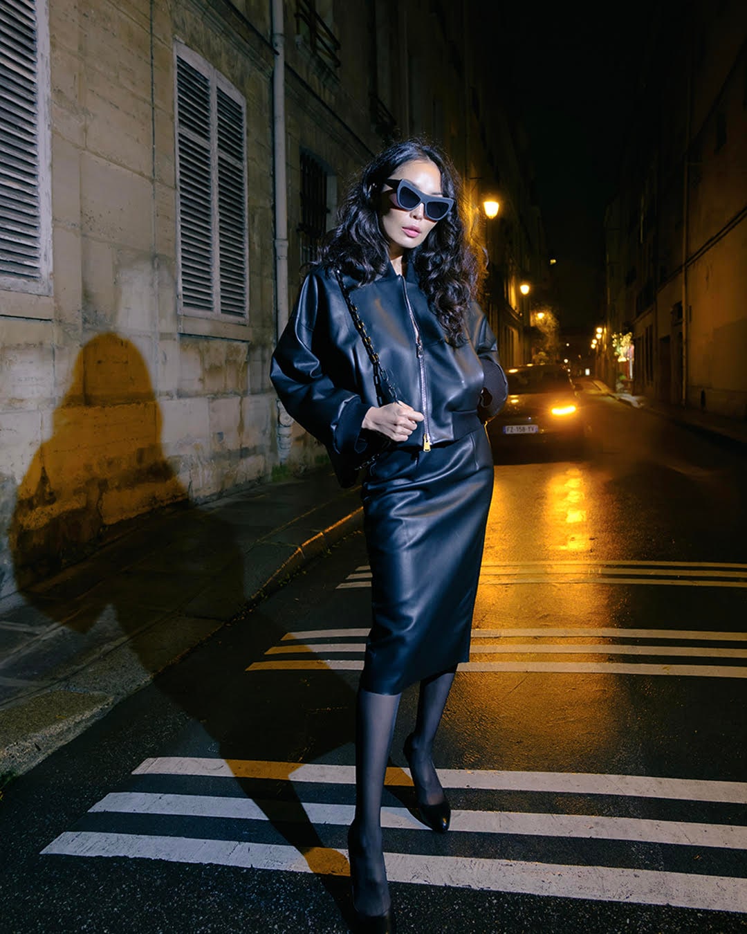 Femme en tenue de cuir noir DEA CULT traversant une rue de Paris la nuit
